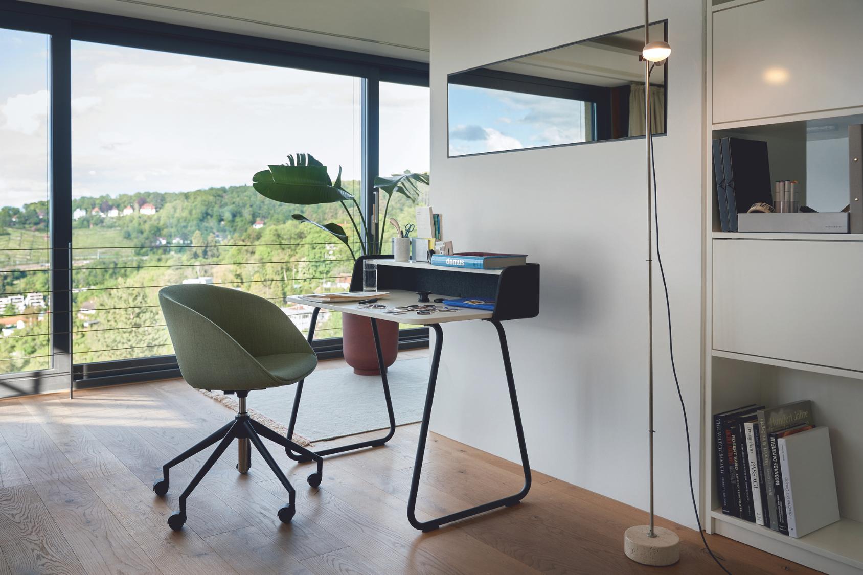 on spot cosy Bürostuhl mit grünem Stoffbezug und schwarzem 5-Stern-Kunststoffgestell vor einem modernen Schreibtisch in einem hellen Raum mit großem Fenster und Blick ins Grüne