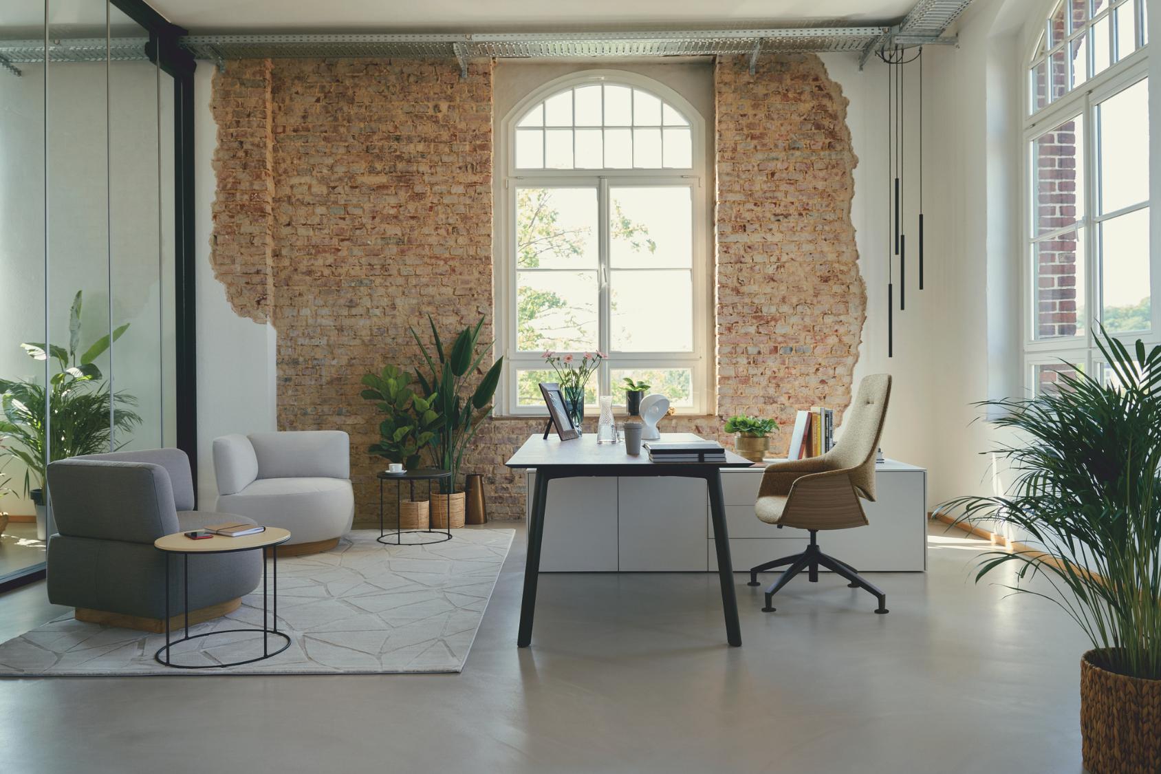 se:mission Bürostuhl mit beige gepolstertem Sitz und Rückenlehne, verstellbar, vor einem Schreibtisch in modernem Loft-Büro mit Backsteinwand und großen Fenstern