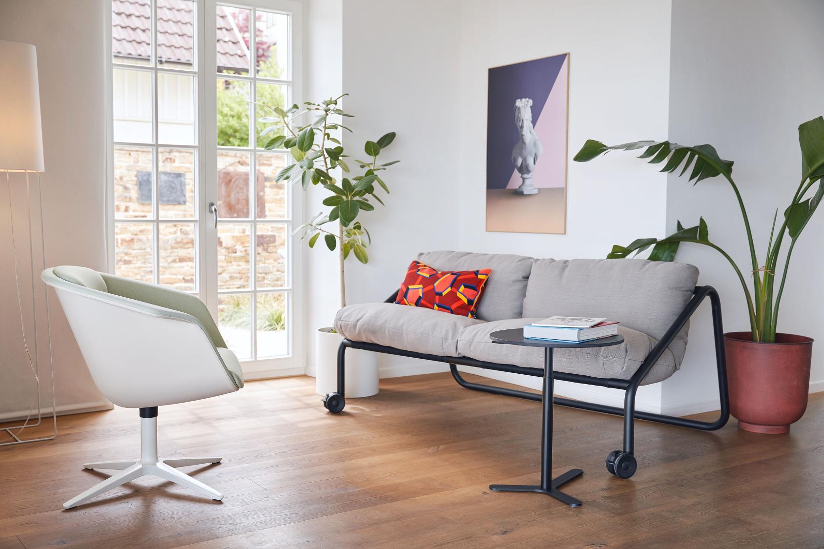 Der sweetspot in hellgrün mit drehbarem Fuß steht im Mittelpunkt eines modernen Wohnzimmers mit grauem Sofa, buntem Kissen und Pflanzen