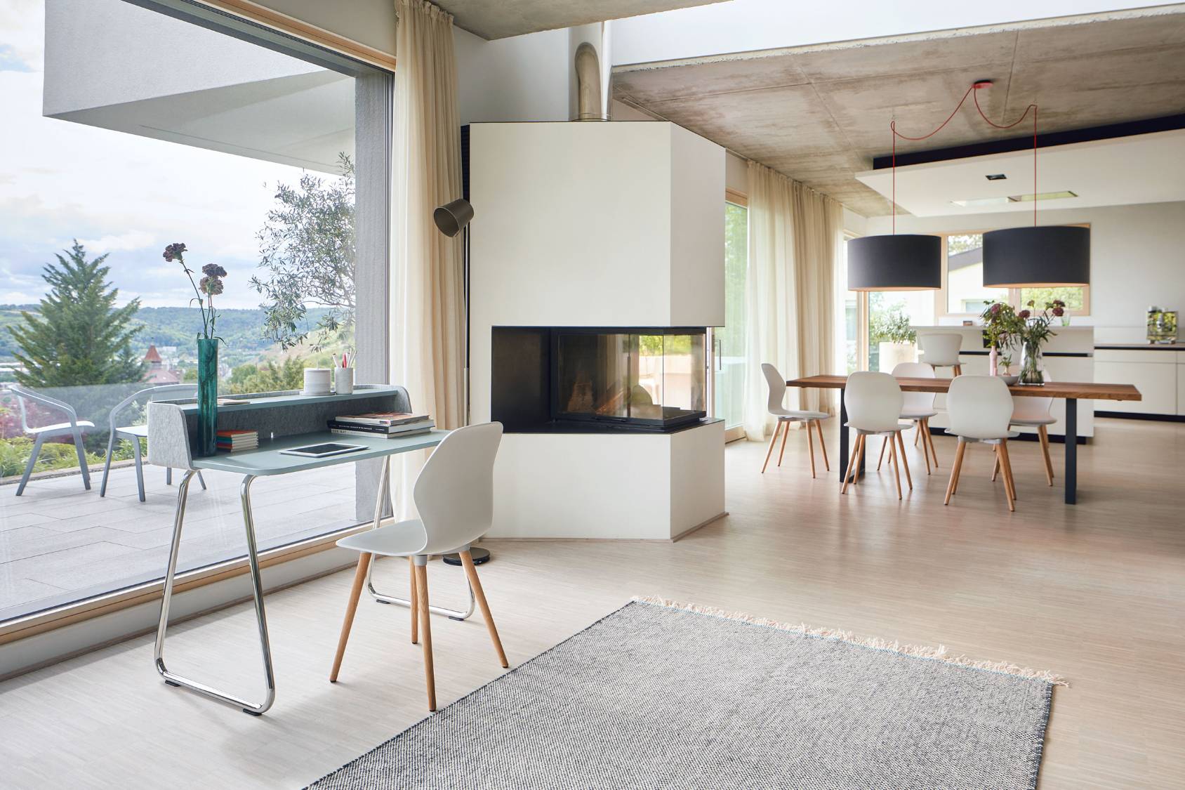 Moderner Essbereich mit großem Holztisch und drei schwarzen se:spot Pendelleuchten mit rundem Design, zwei Personen im Gespräch, eine sitzt mit Laptop am Tisch