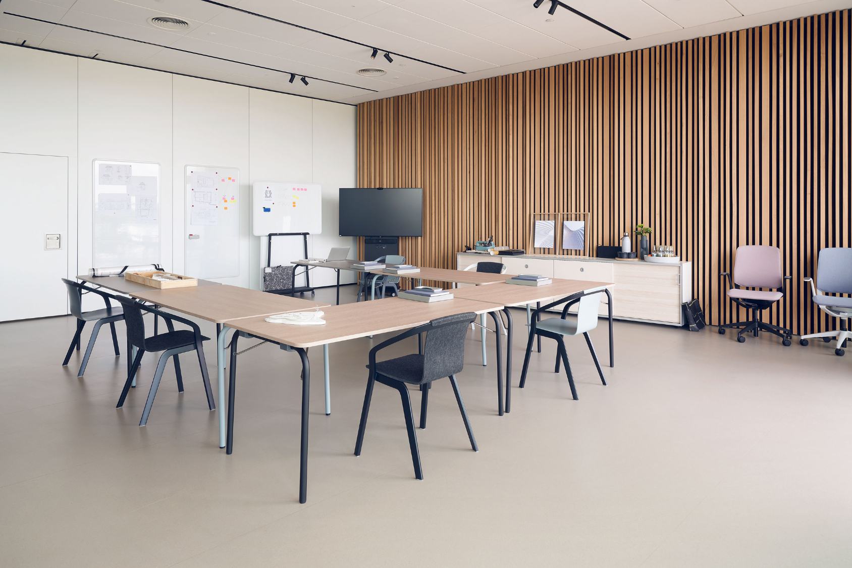 Moderner Besprechungsraum mit mehreren se:mood Stühlen um helle Holztische, weiße Wände und Holzlamellenwand im Hintergrund
