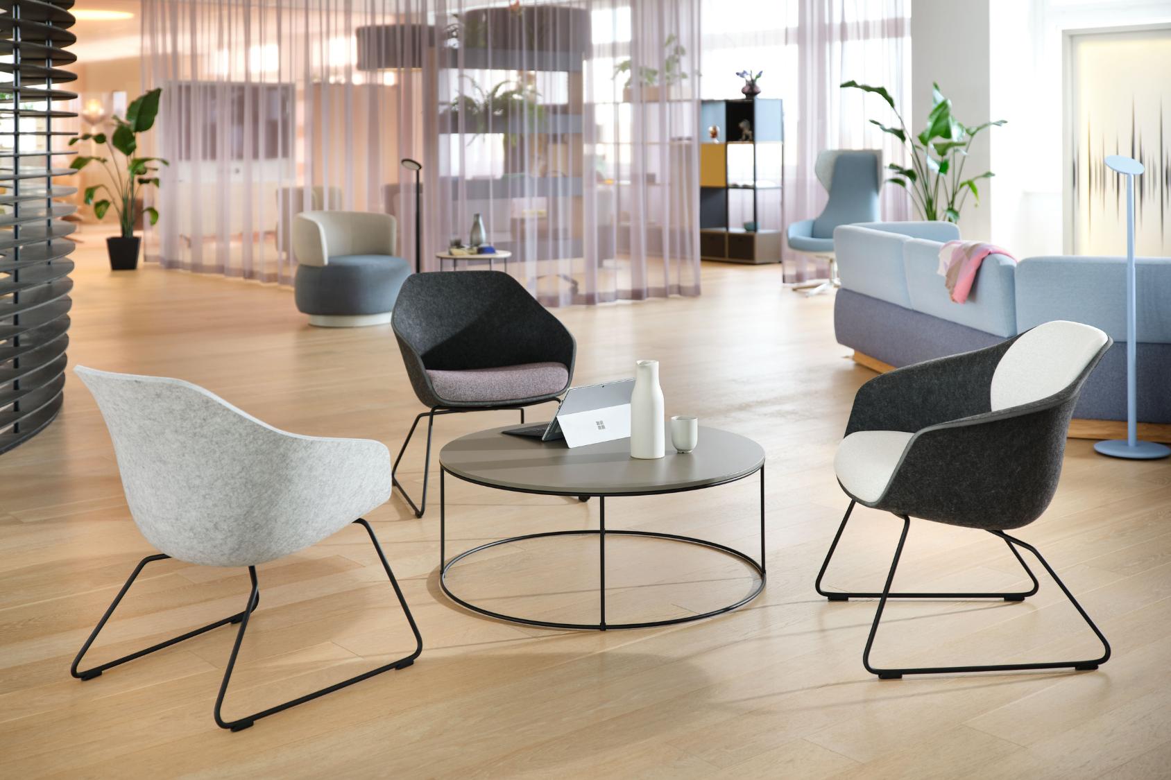 Drei se:lounge light Bürostühle mit schwarzem Metallgestell und gepolsterten Sitzen in Grau- und Weißtönen um einen runden Couchtisch in einem modernen, hellen Büro mit Holzfußboden