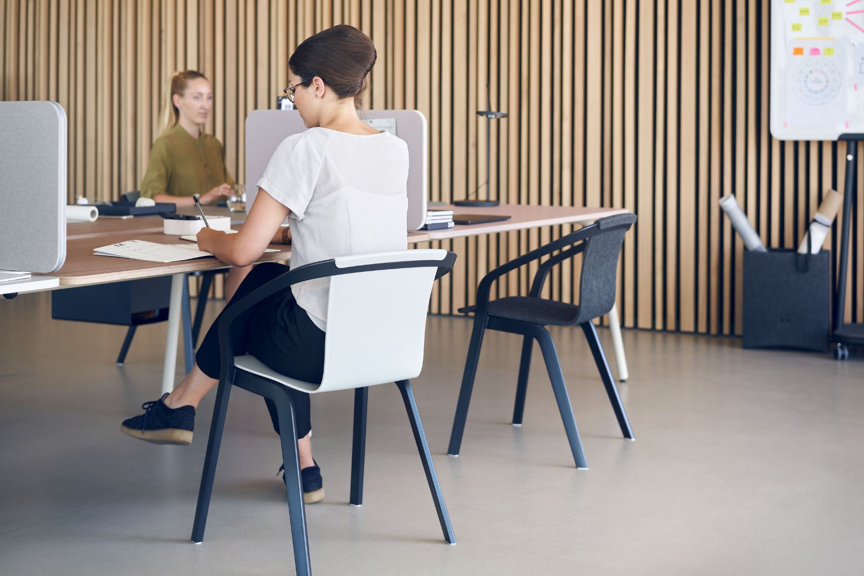 Der se:mood mit schwarzem Gestell und weißer Rückenlehne, besetzt von einer sitzenden Person in einem modernen Büro mit Holzwandverkleidung