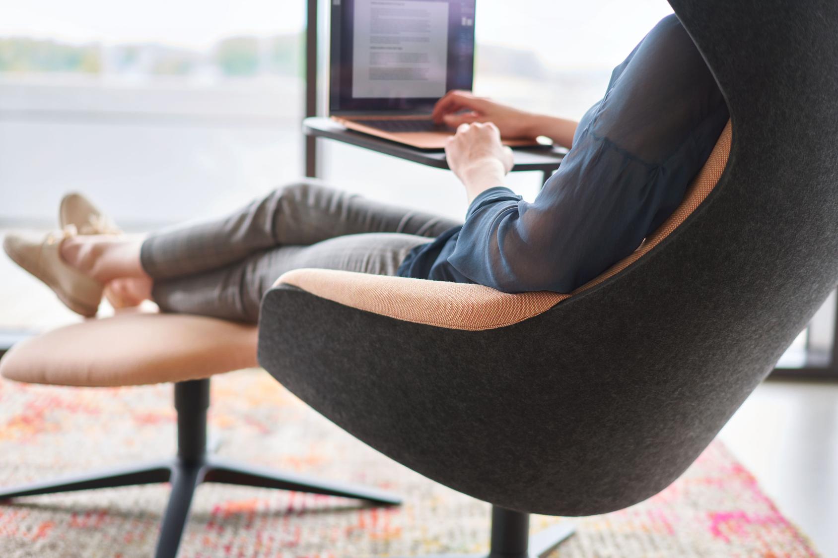 Person sitzt entspannt im se:lounge Ottoman Fußhocker und arbeitet an einem Laptop