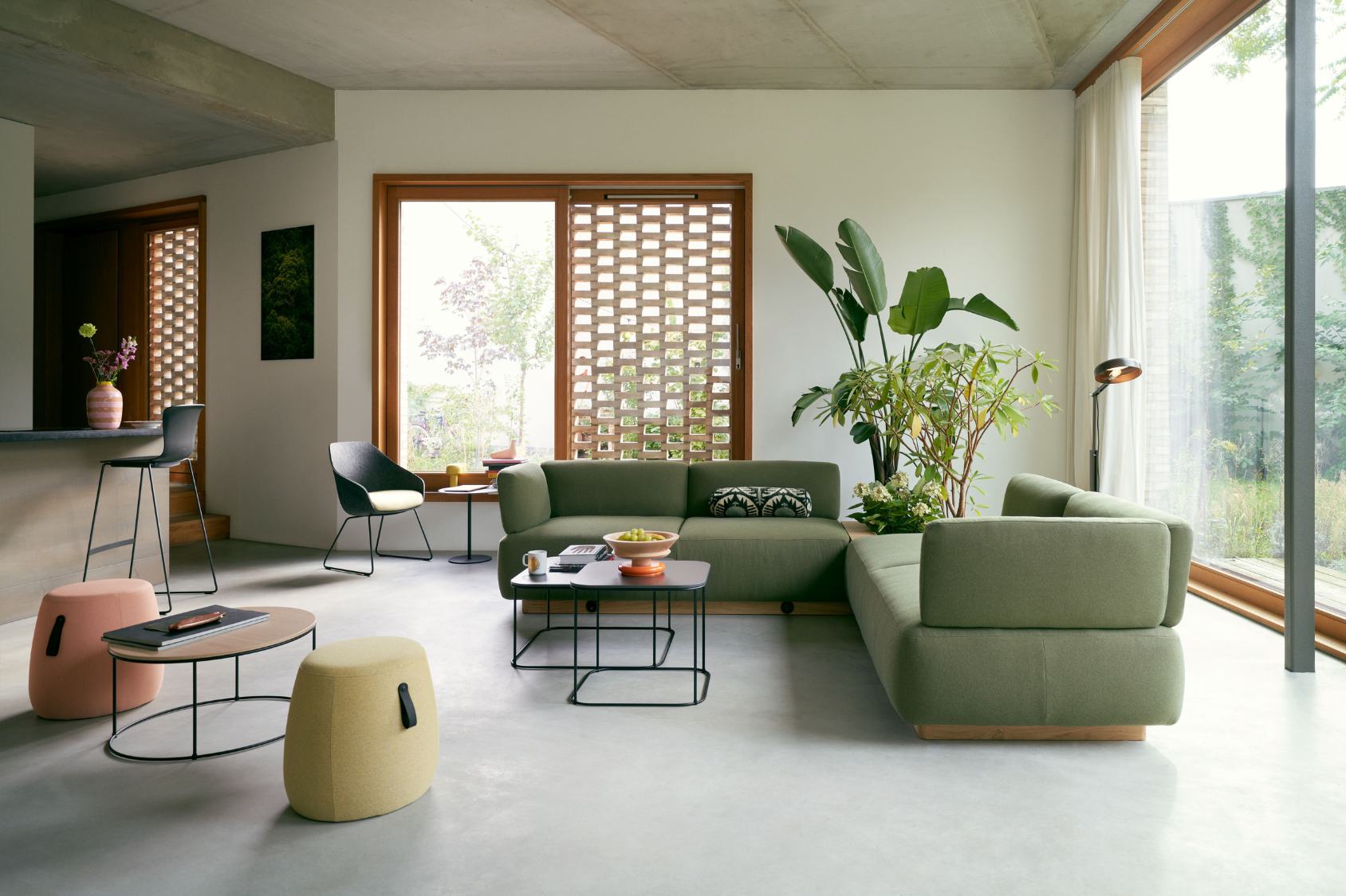se:living Sofa als grünes Ecksofa mit klaren Linien und Holzsockel in modernem Wohnzimmer mit großen Fenstern und Pflanzen