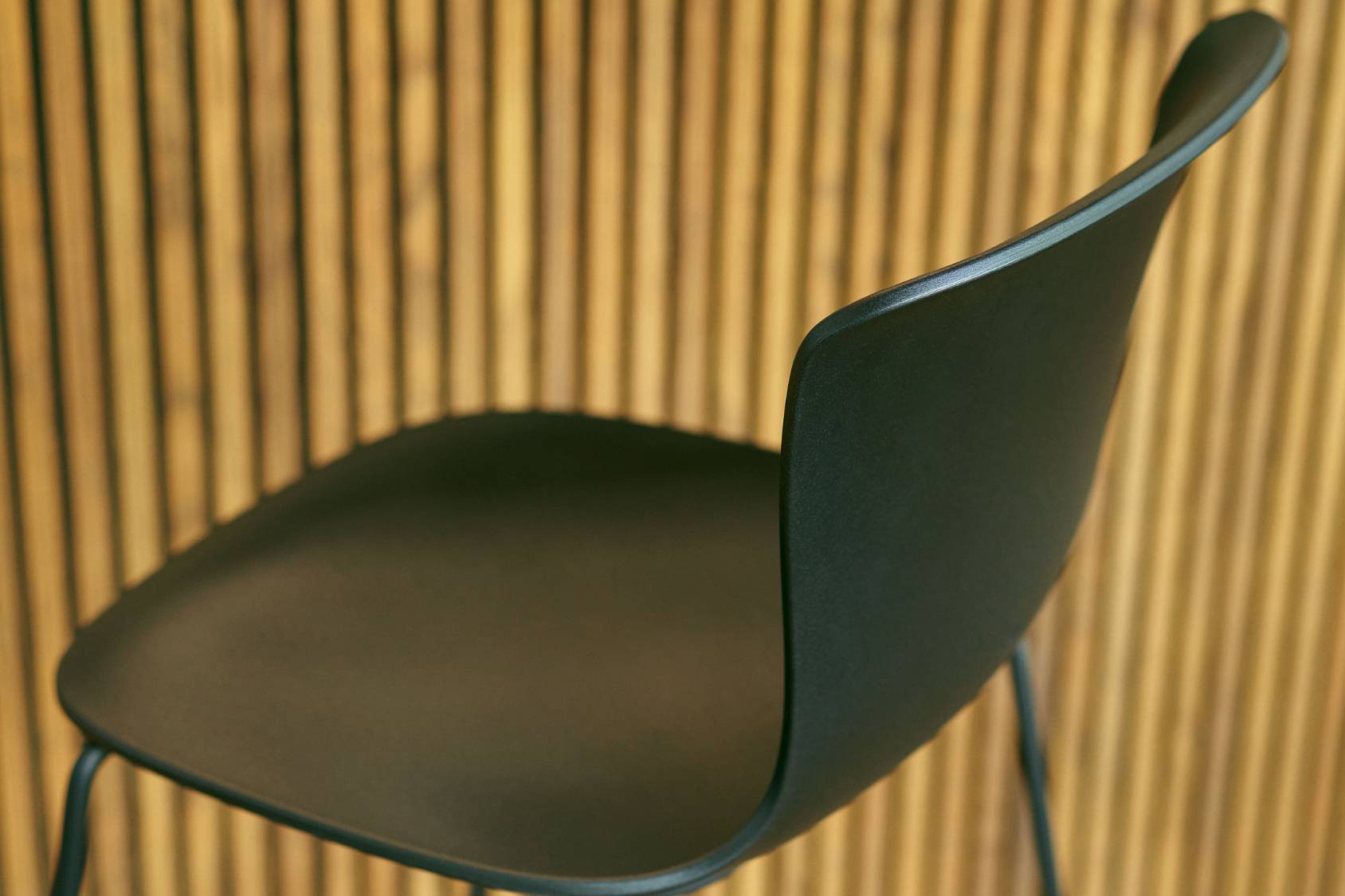 se:spot stool Barhocker mit ergonomisch geformter, schwarzer Sitzschale und schlanken Metallbeinen vor Holzlamellenwand